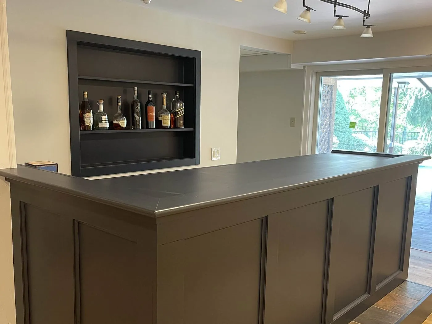 The finished lower-level bar with a paneled front, a dark top and the built-in shelves stocked with bottles