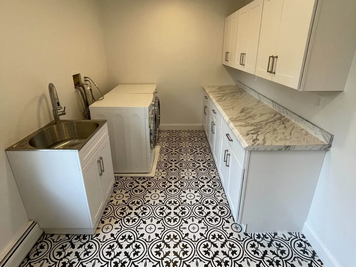 The finished laundry room with white upper and lower cabinets, a stone counter, a utility sink and the washer and dryer