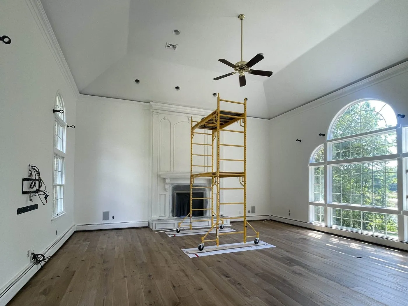 Great room before painting, with a white fireplace surround and scaffolding set up for the high ceiling