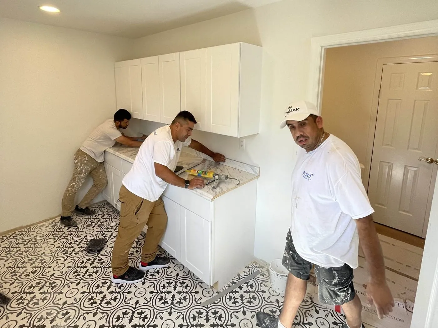 Paint Plus crew installing new white shaker cabinets and a stone counter in a laundry room with a patterned tile floor