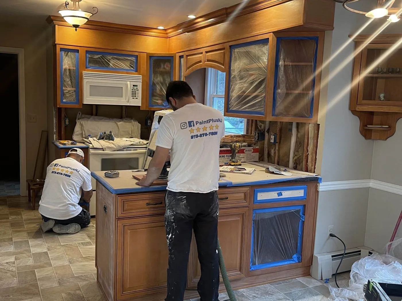 Kitchen with honey oak cabinets taped off and protected, while the Paint Plus crew prepares them for painting