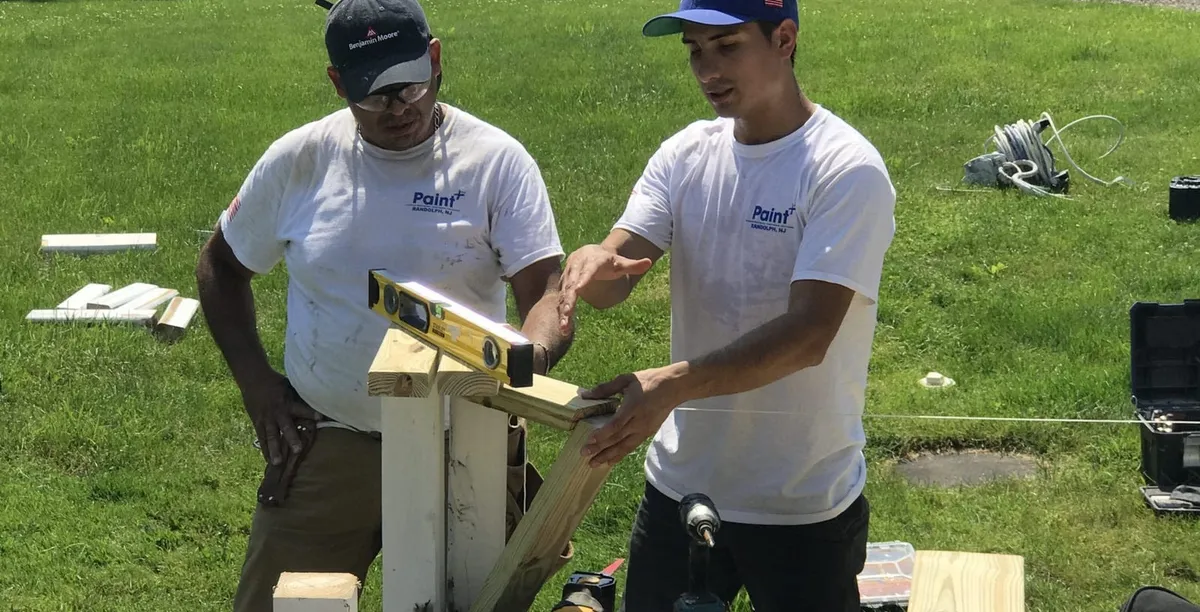 Paint Plus owner John Reyes and a crew member leveling a post on a new deck build
