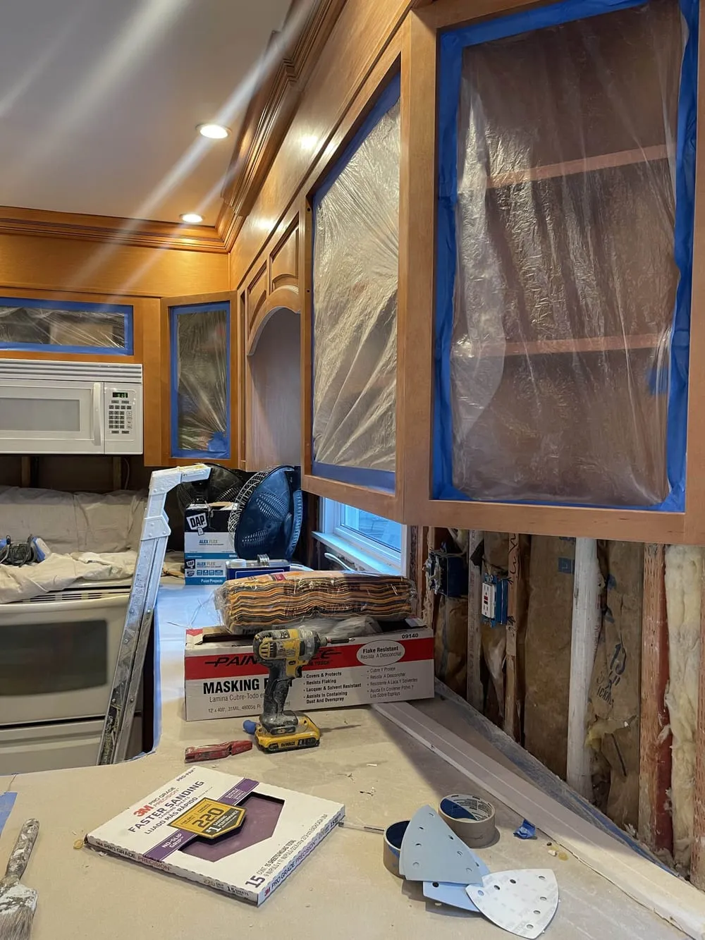 Upper cabinets with glass fronts masked in plastic and blue tape, ready for spraying