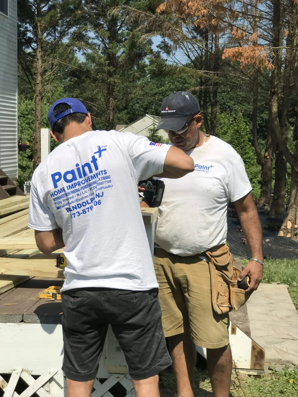 Two Paint Plus crew members building a new deck railing in a backyard