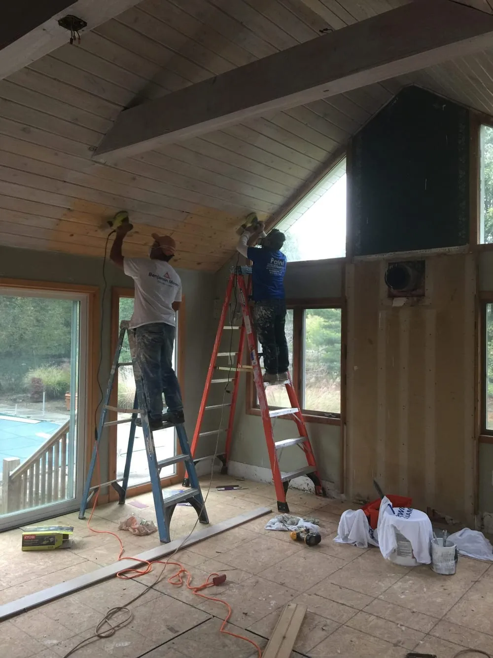 Two Paint Plus painters on ladders painting a vaulted wood plank ceiling