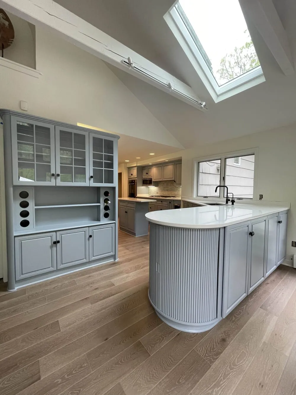Curved kitchen island with a fluted end panel and white countertop under a skylight