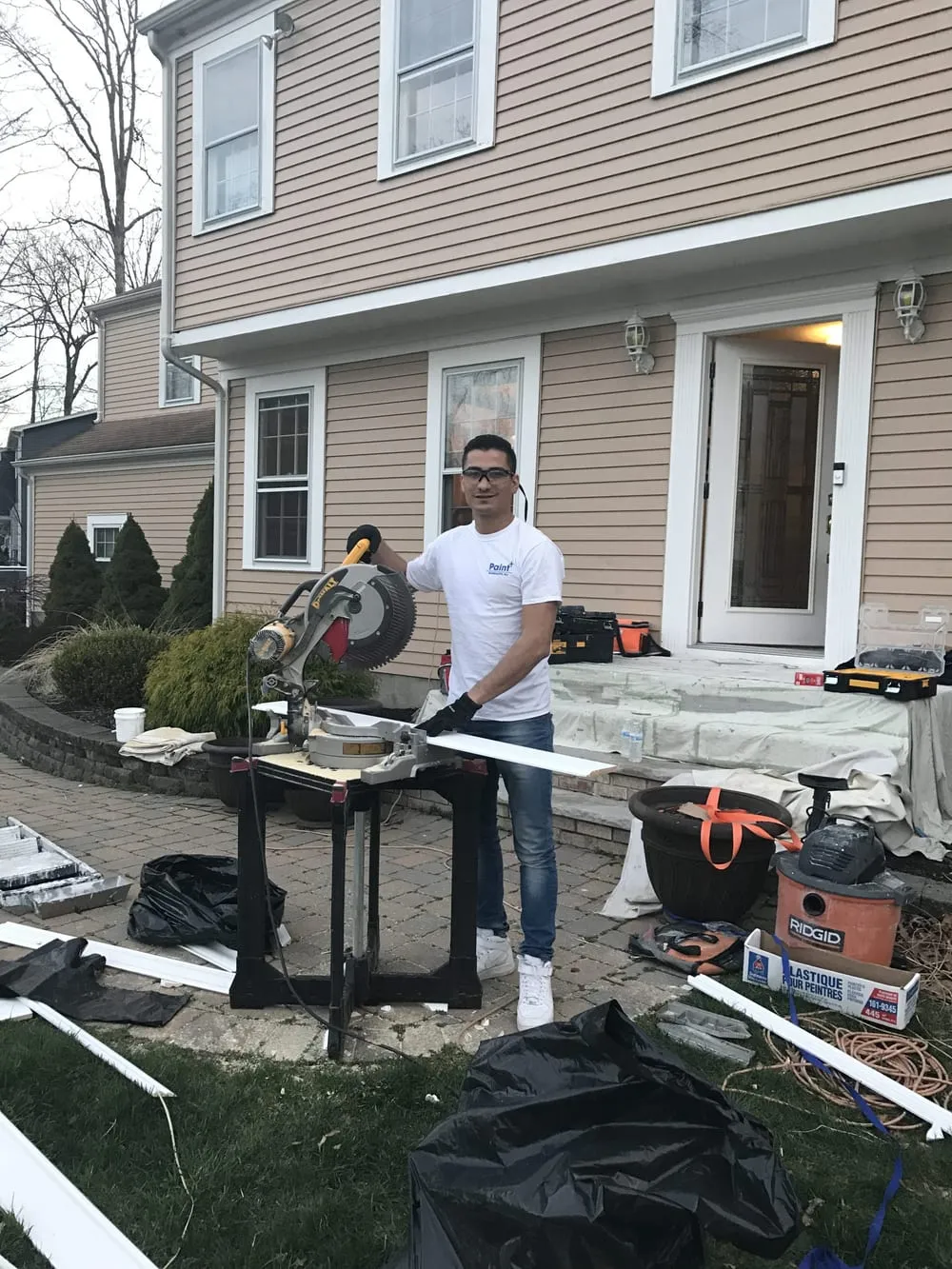 Paint Plus crew member cutting new exterior trim boards with a miter saw outside a house