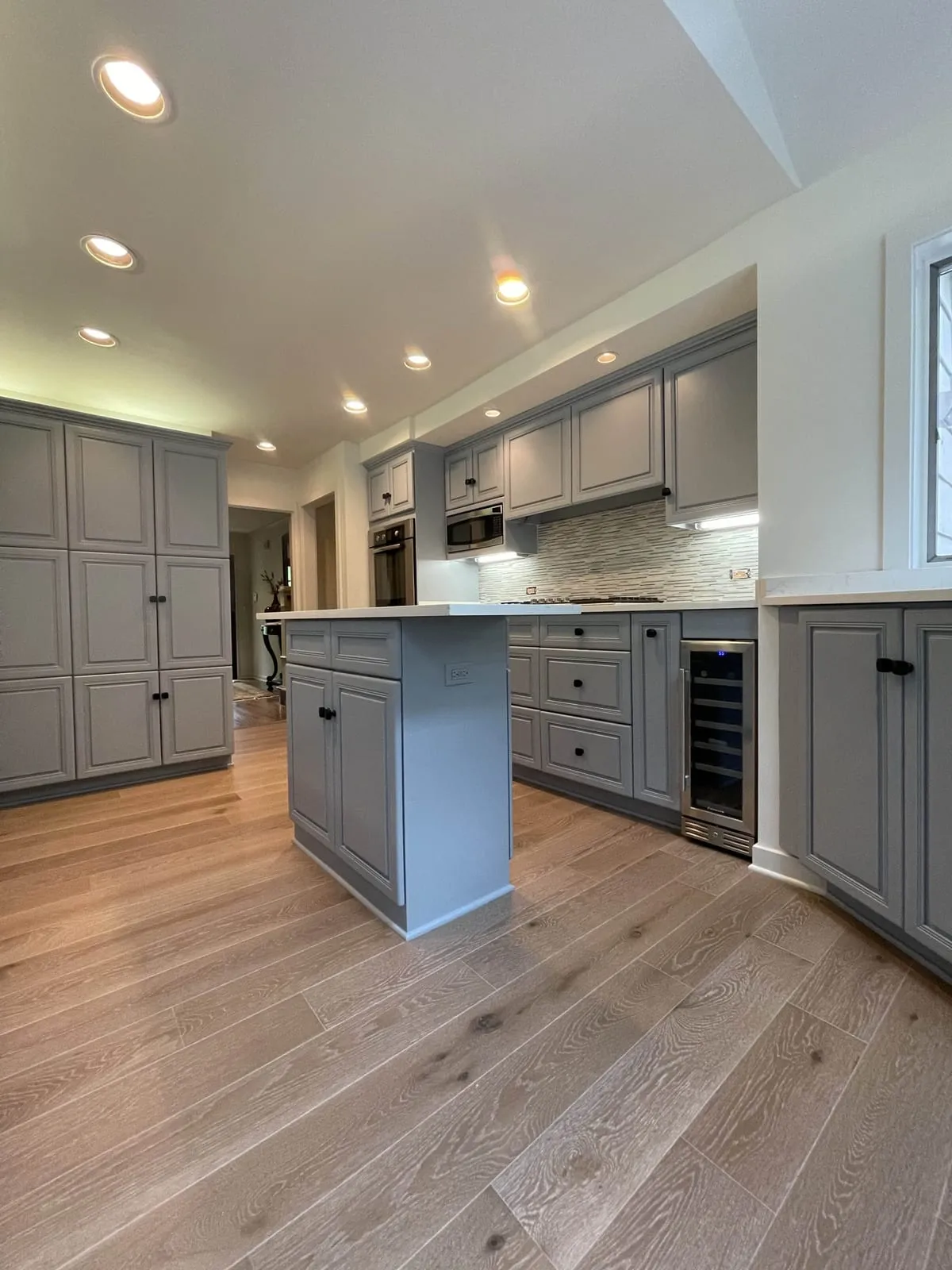 Kitchen with gray raised-panel cabinets, a white-topped island, a mosaic backsplash and wide-plank oak floors