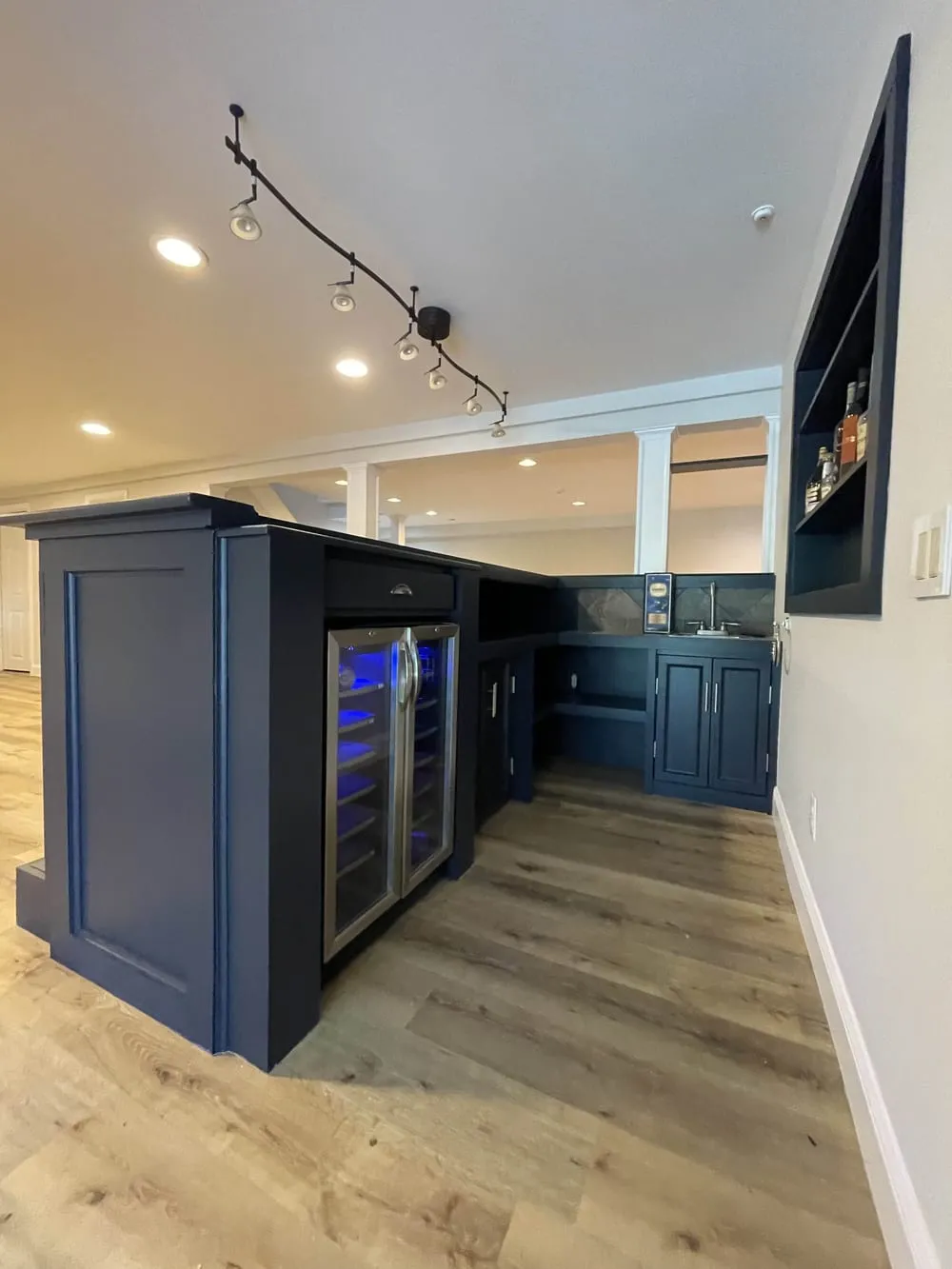 Navy home bar with a lit built-in wine fridge and matching cabinetry, on new plank flooring
