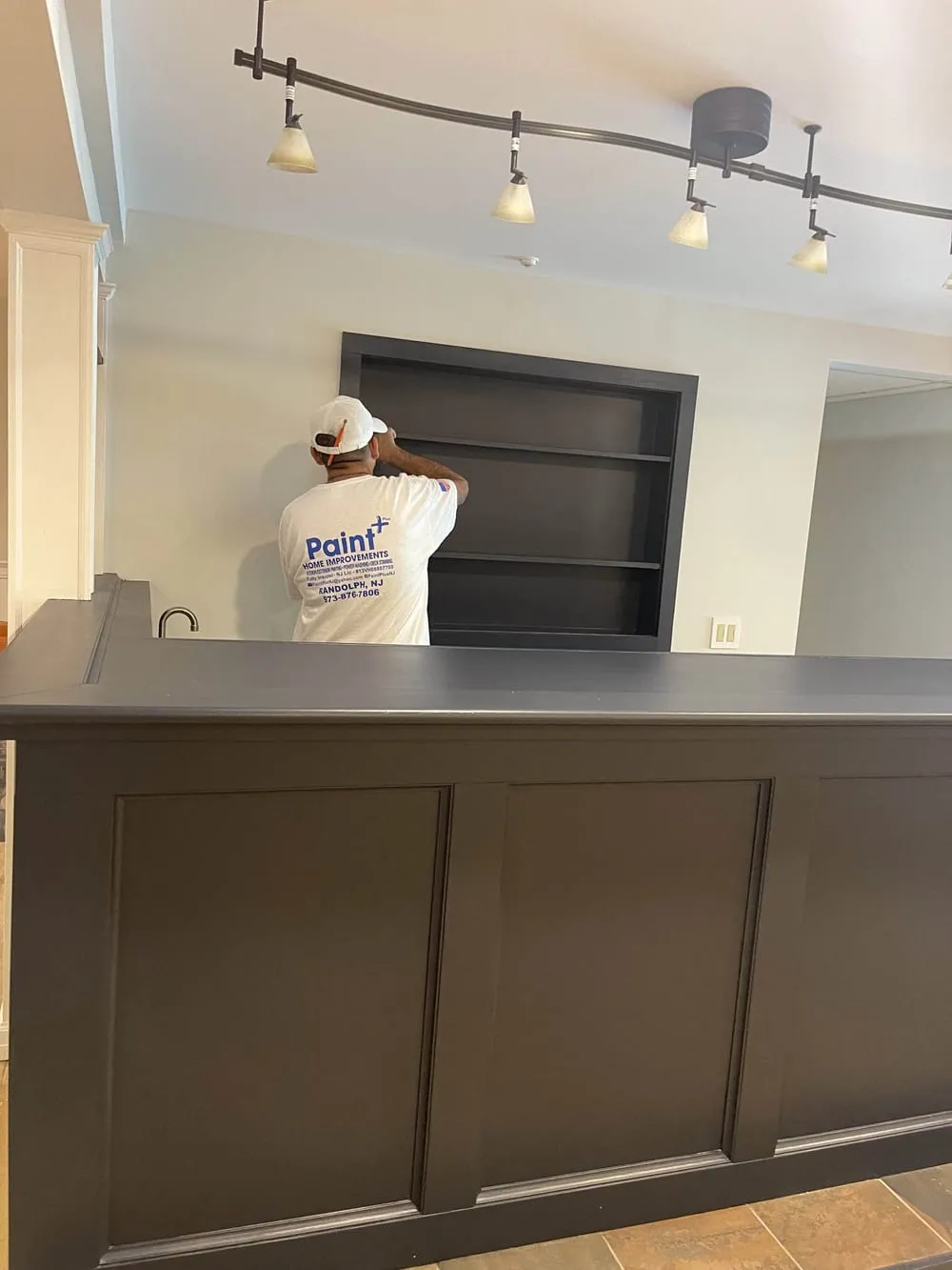 Paneled front of a custom home bar painted dark gray, with built-in shelving behind it
