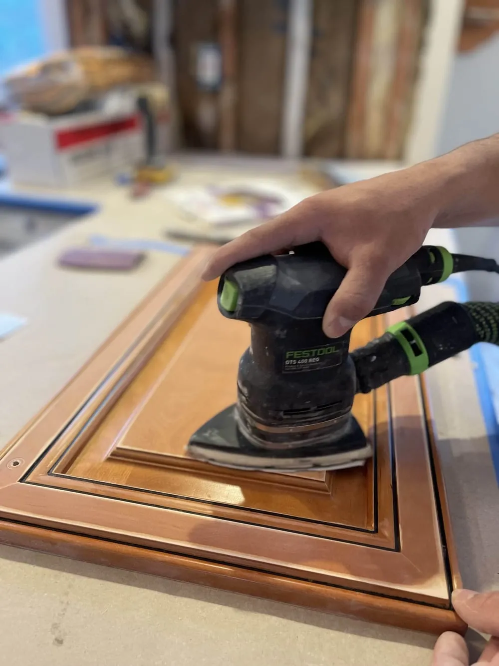Close-up of a raised-panel oak cabinet door being sanded before priming