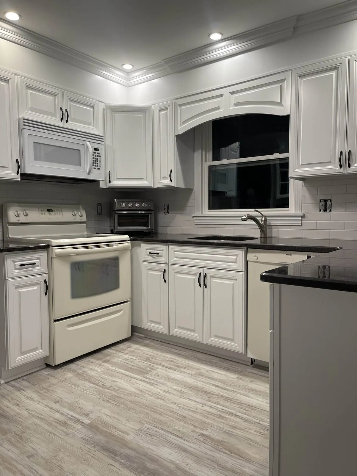 Finished kitchen with white painted cabinets, an arched valance over the sink window and a white subway tile backsplash