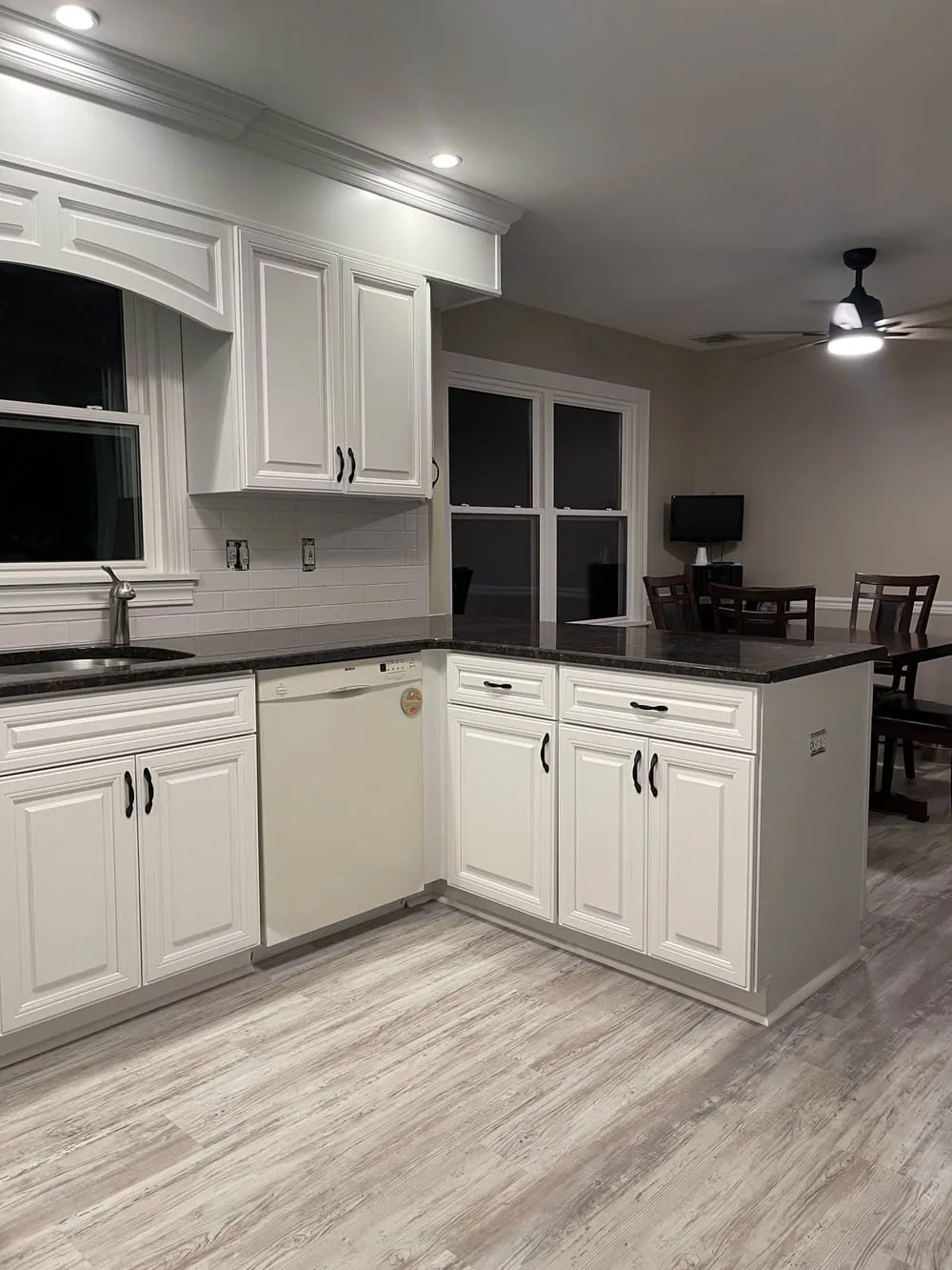 White painted kitchen with a dark granite peninsula opening into the dining area