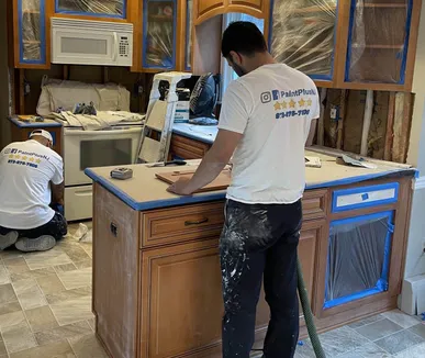 Paint Plus crew refinishing wood kitchen cabinets, with the kitchen taped off and protected