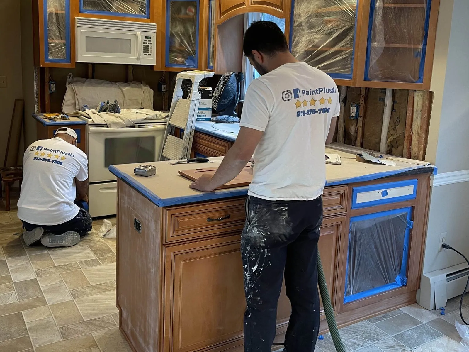 Paint Plus crew refinishing wood kitchen cabinets, with the kitchen taped off and protected