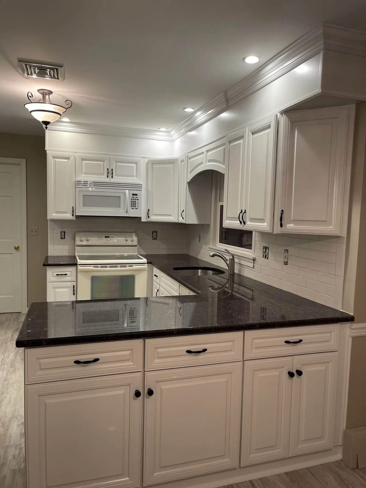 White painted kitchen cabinets with dark granite counters and a subway tile backsplash, by Paint Plus