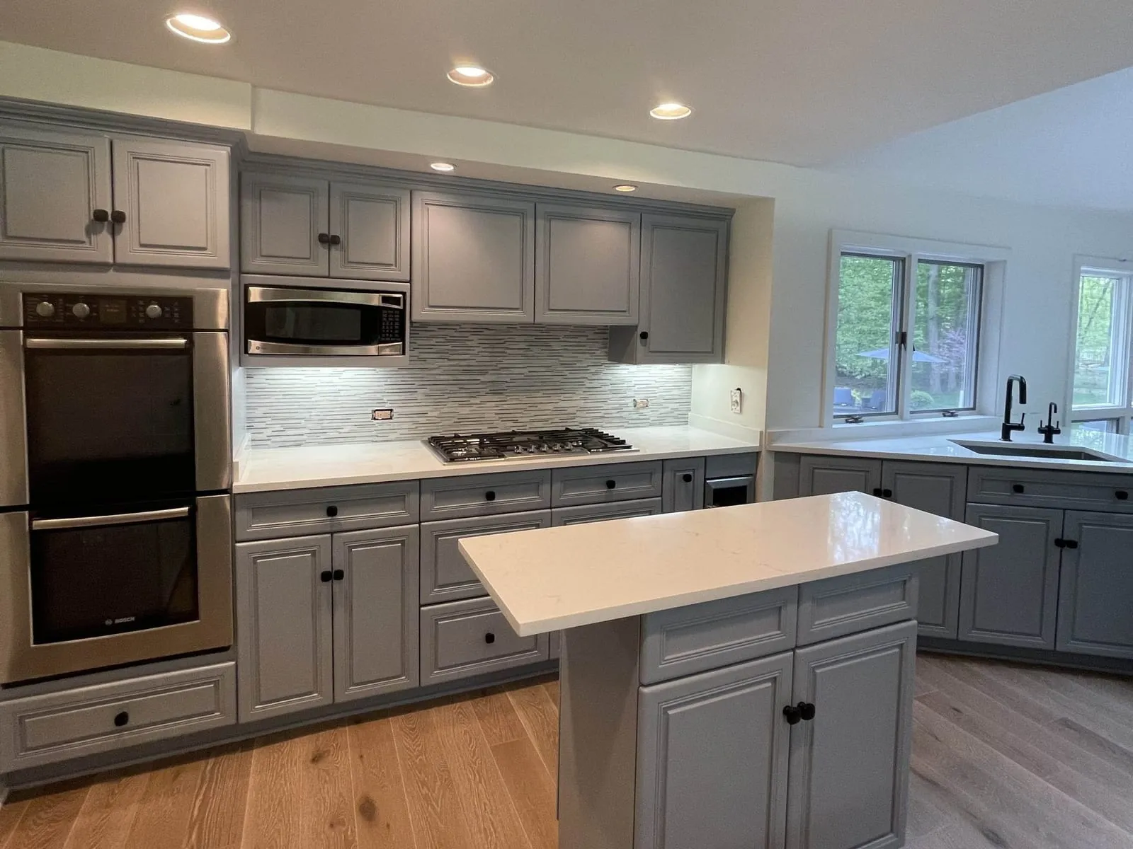 Remodeled kitchen with gray cabinets, a white island and wide-plank wood floors