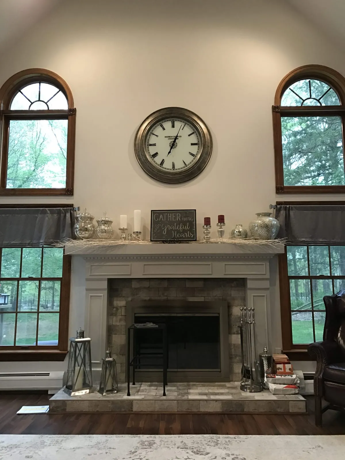 Living room with a painted stone fireplace mantel, a large wall clock and arched windows, by Paint Plus