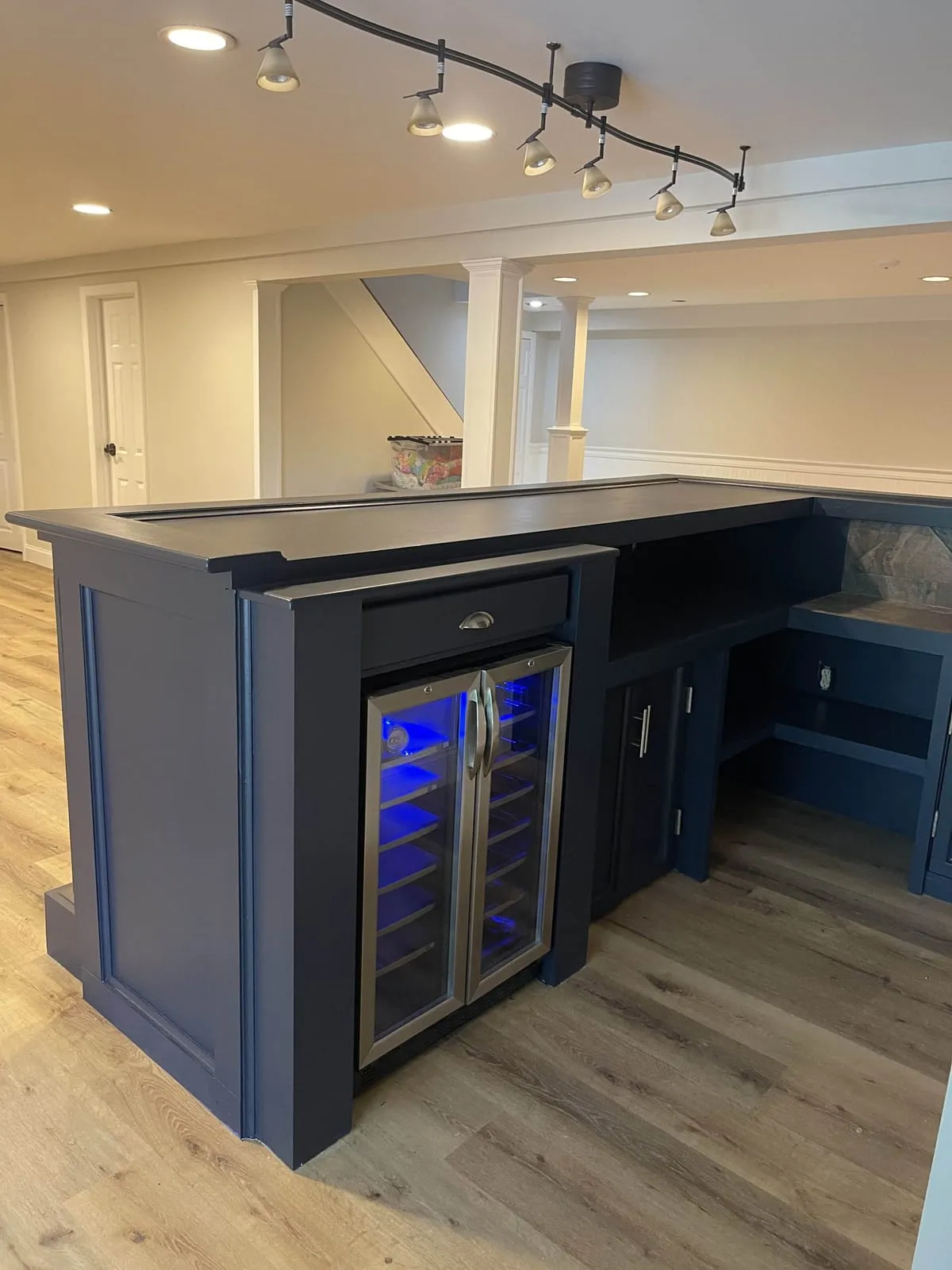 Custom navy basement bar with a built-in wine fridge and matching cabinetry, by Paint Plus