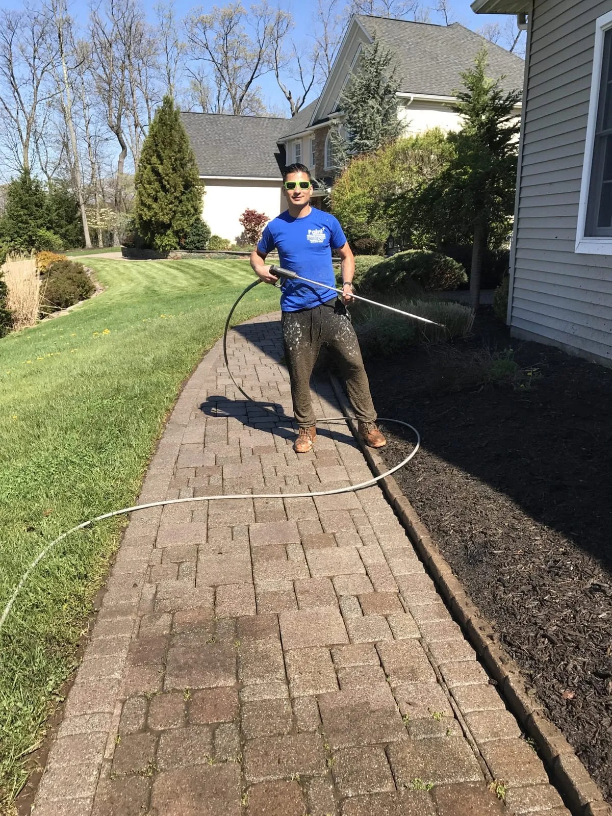 Paint Plus owner John Reyes pressure washing a brick paver walkway beside a house