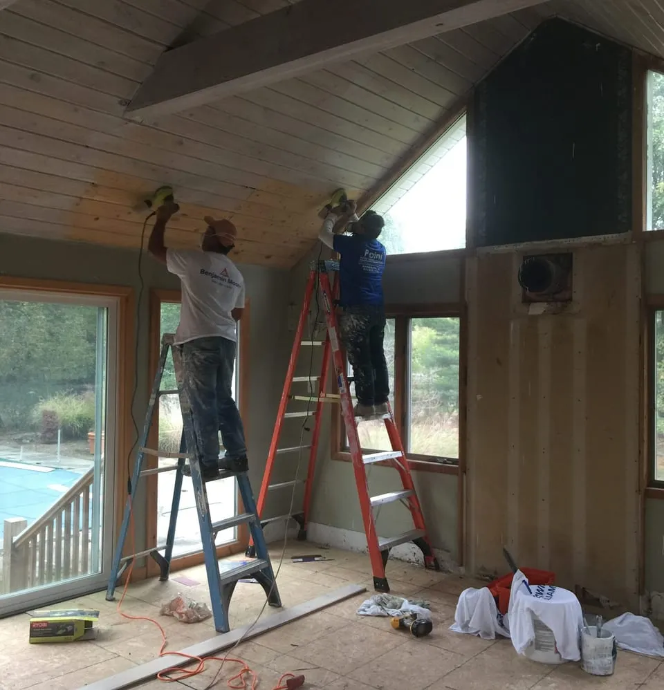 Two Paint Plus painters on ladders painting a vaulted wood plank ceiling in Basking Ridge, NJ