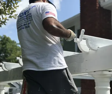 Paint Plus painter rolling white paint on an exterior pergola in Wharton, NJ