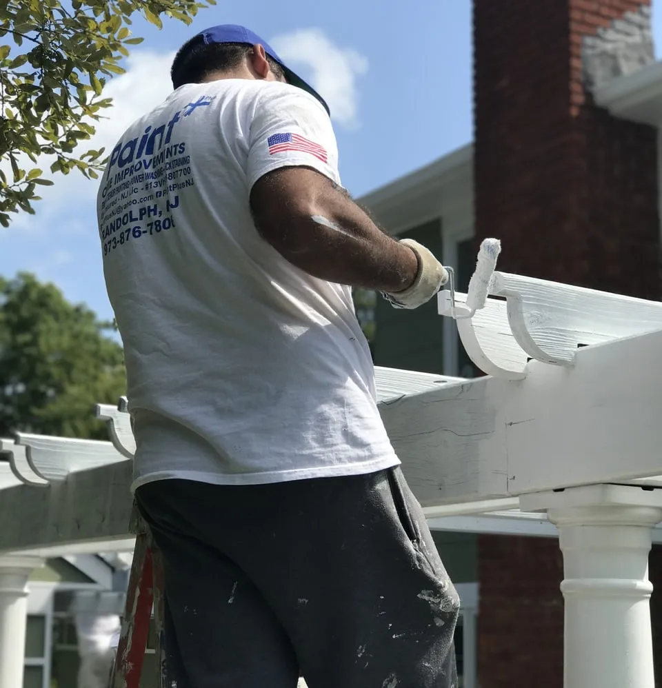 Paint Plus painter rolling white paint on an exterior pergola in Wharton, NJ