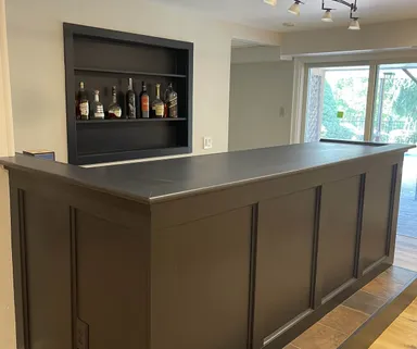 Custom basement bar with a painted paneled front and built-in shelves, built by Paint Plus