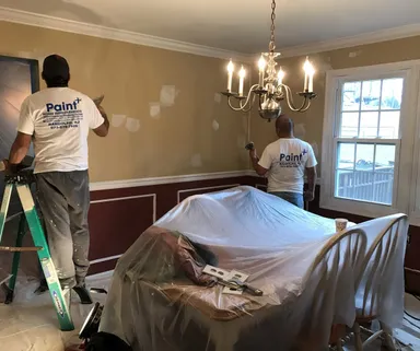 Two Paint Plus painters prepping dining room walls with the furniture covered in plastic